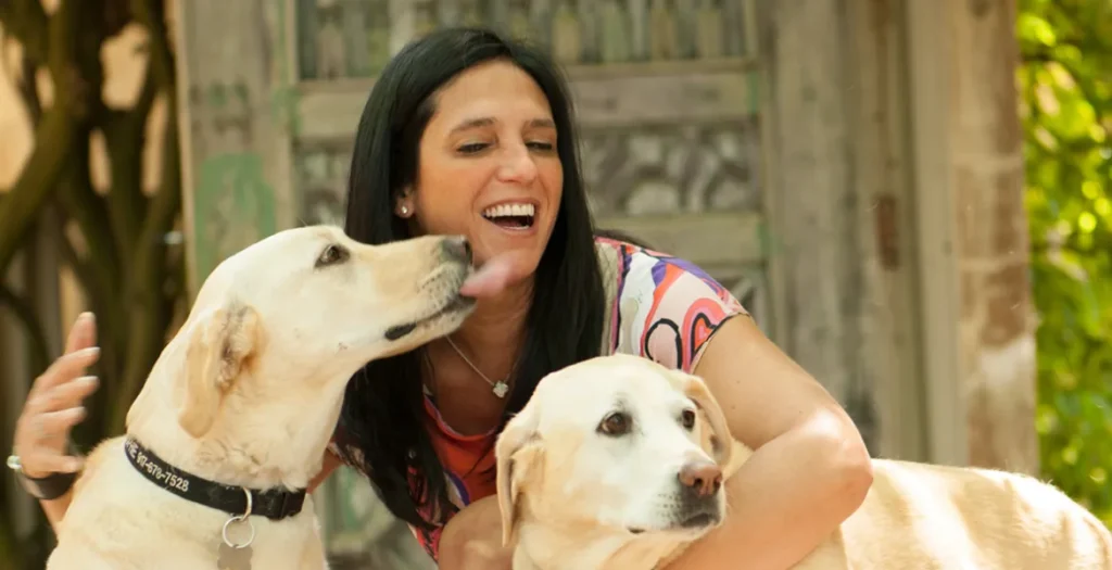 Woman smiling with two dogs licking her face.